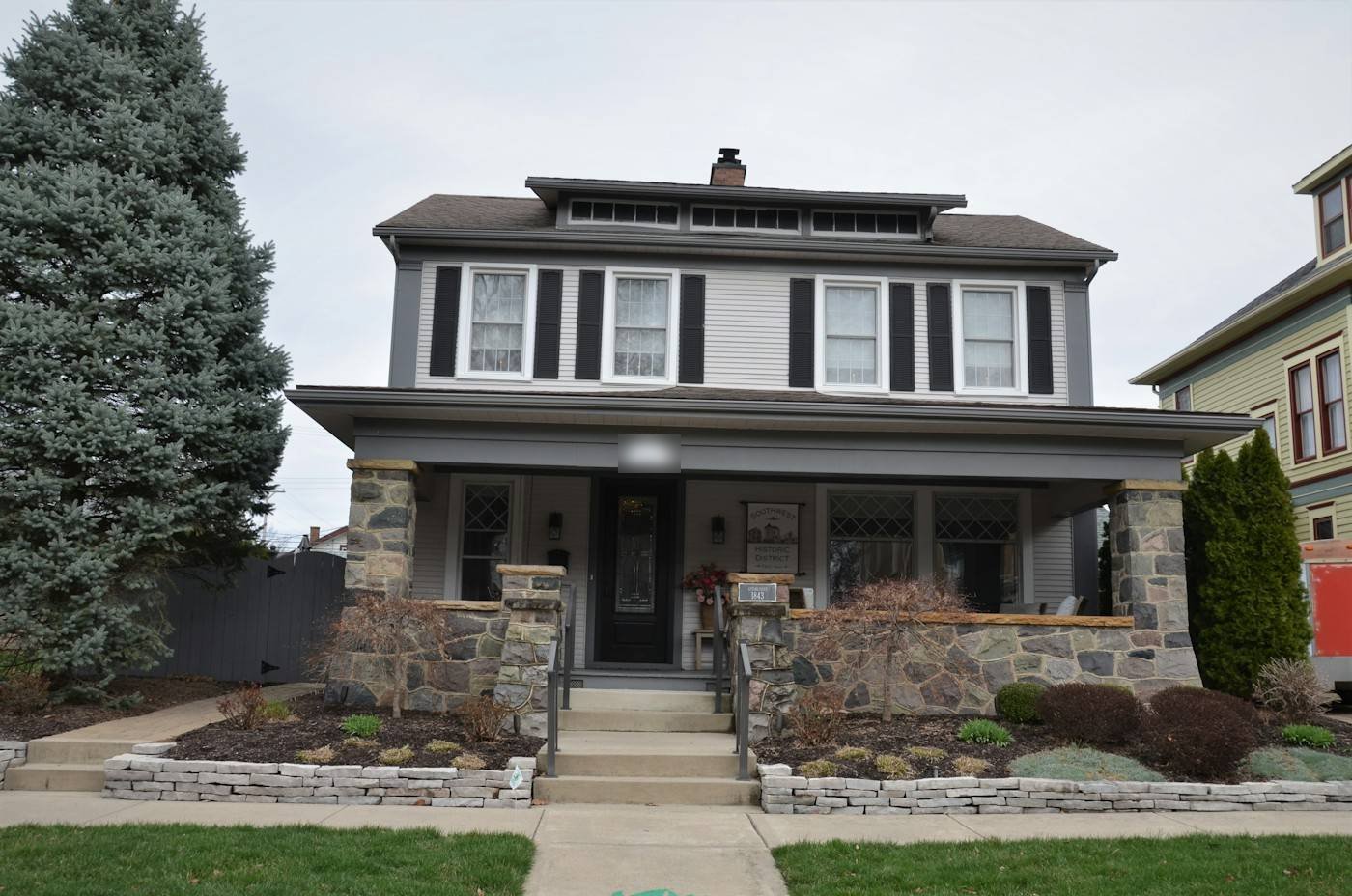 A gray two-story house with a stone porch and black shutters