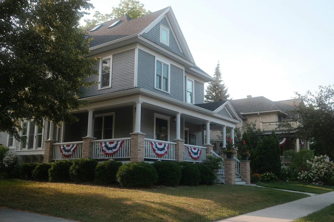 A gray two-story house with a wraparound porch and brick piers