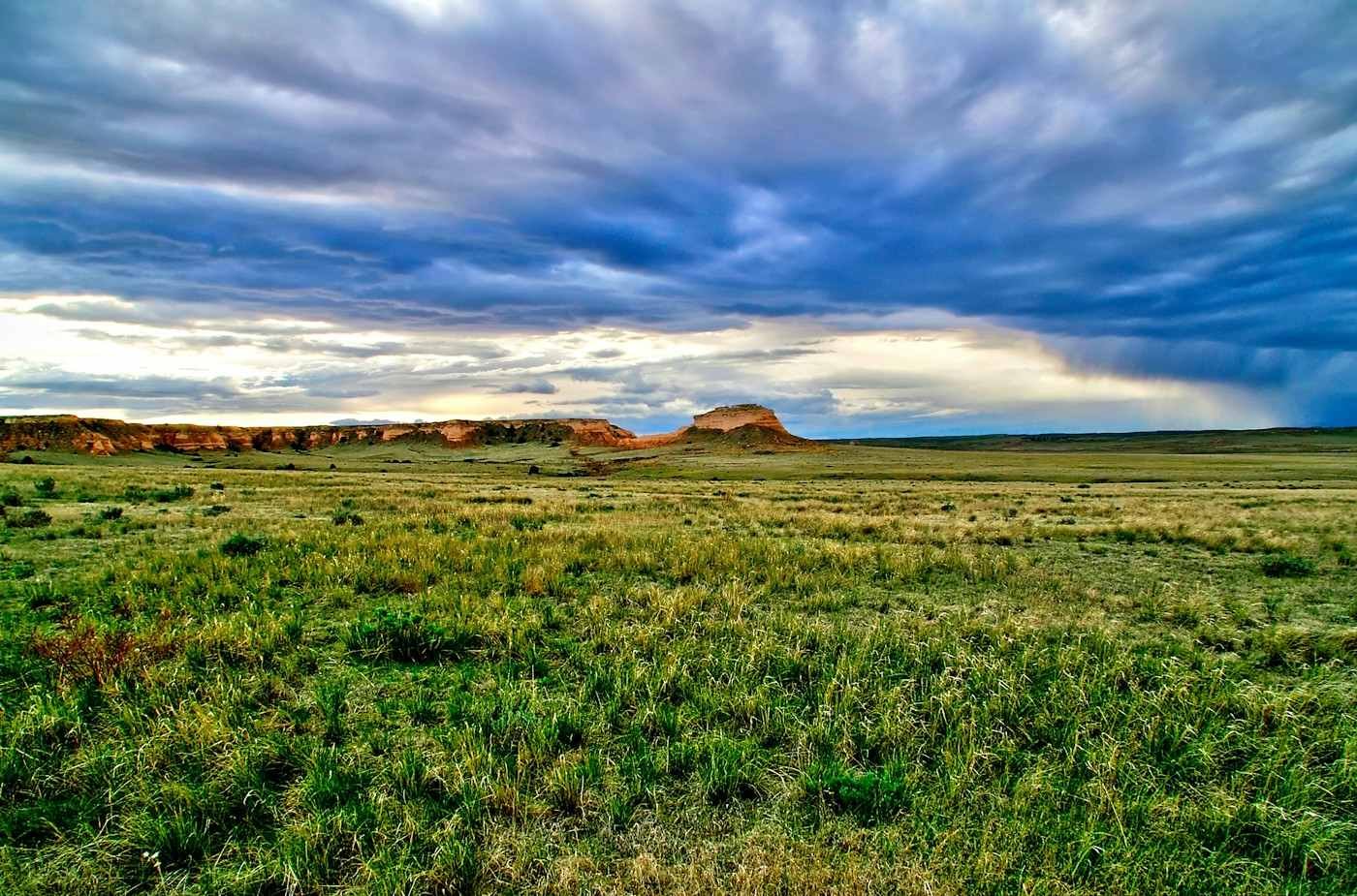 Green prairie and low buttes under a streaked evening sky