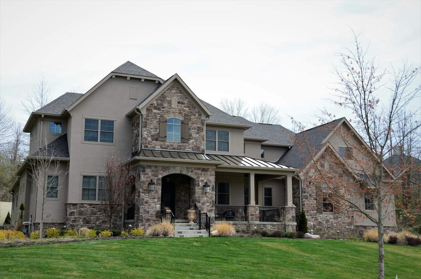 A stone and stucco two-story home with a dark shingle roof