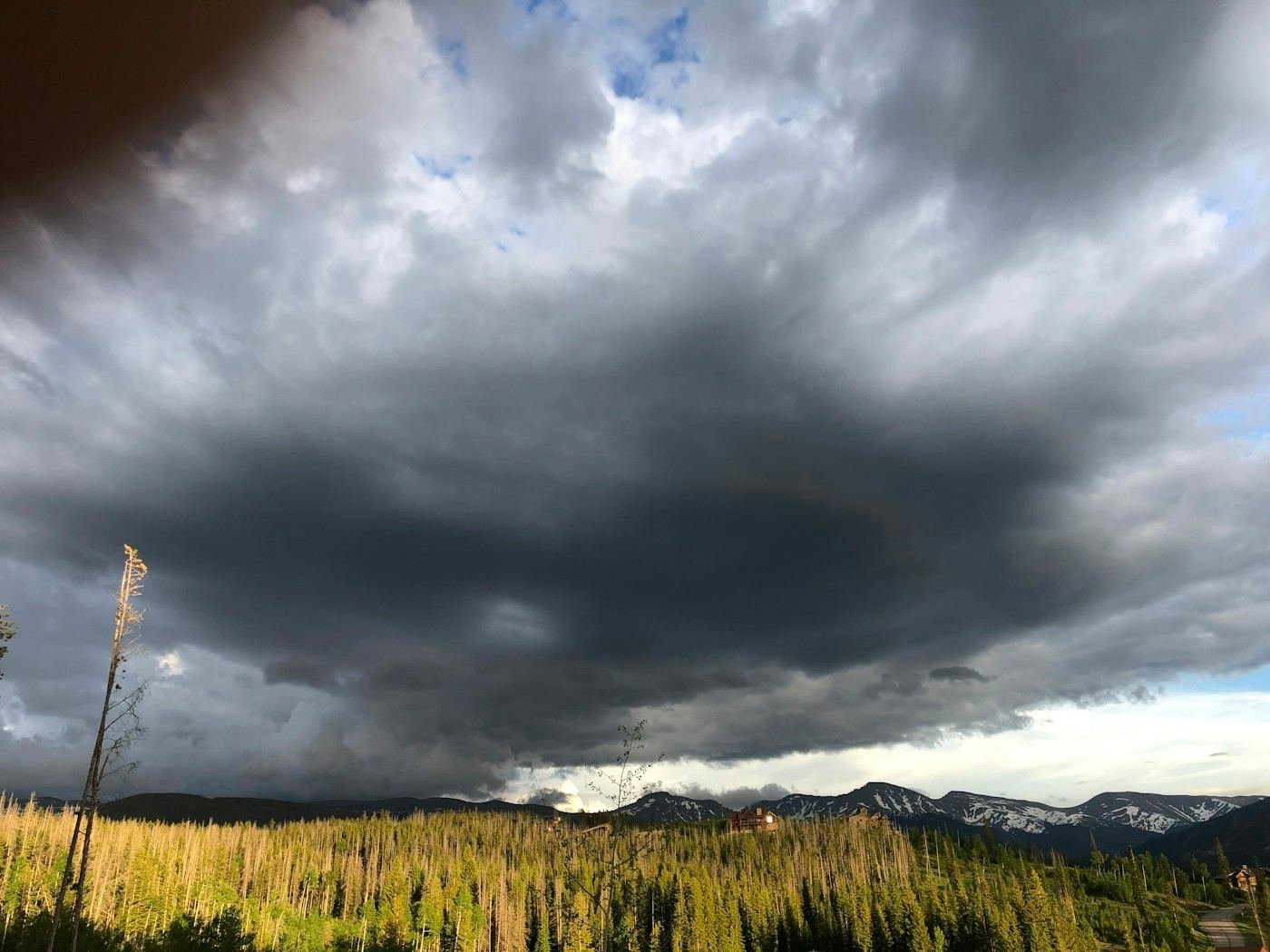 A dark storm cloud over pine-covered foothills